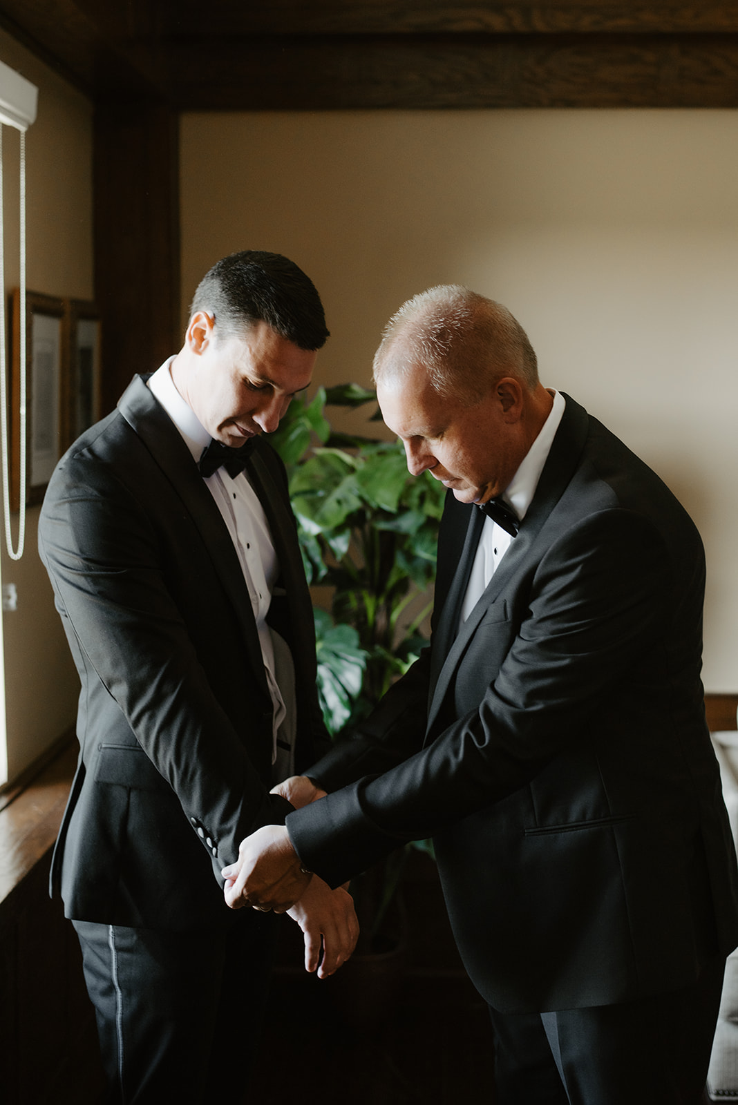 Father in tuxedo adjusting the groom's sleeve in a quiet bonding moment before the ceremony.